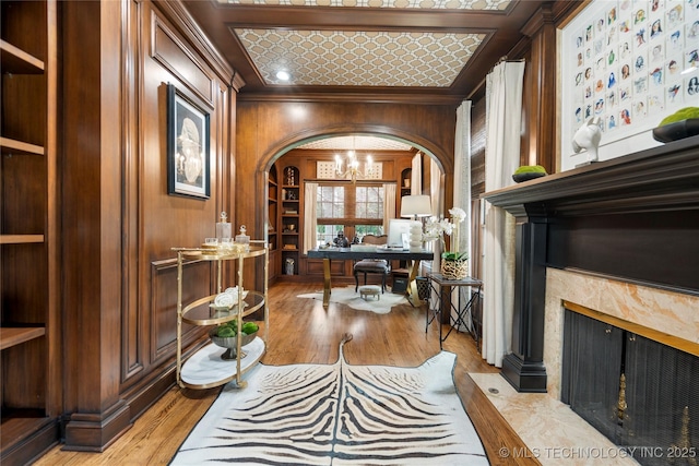 interior space featuring arched walkways, a fireplace, wood walls, a chandelier, and ornamental molding
