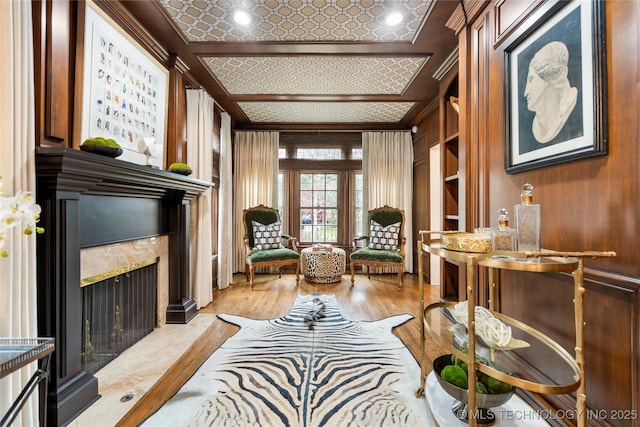 sitting room featuring wood walls, ornamental molding, a fireplace, built in shelves, and light wood-style flooring