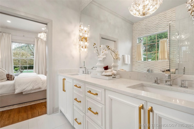ensuite bathroom with connected bathroom, double vanity, a notable chandelier, and a sink