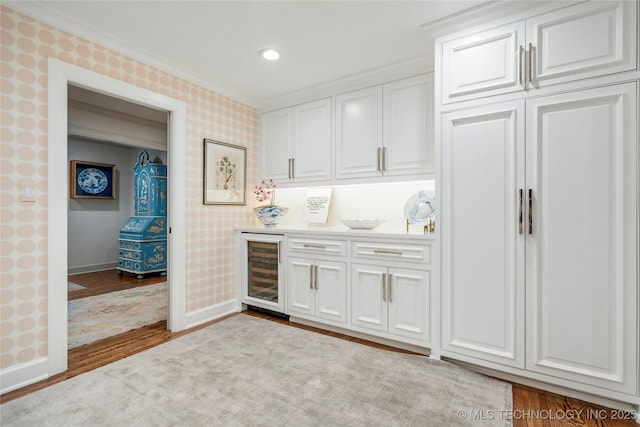 bar with ornamental molding, wood finished floors, beverage cooler, baseboards, and wallpapered walls