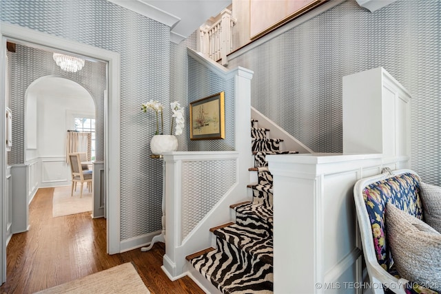 stairs featuring arched walkways, wood finished floors, baseboards, an inviting chandelier, and wallpapered walls