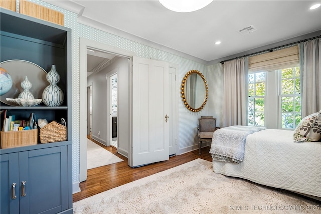 bedroom featuring visible vents, wood finished floors, baseboards, ornamental molding, and wallpapered walls