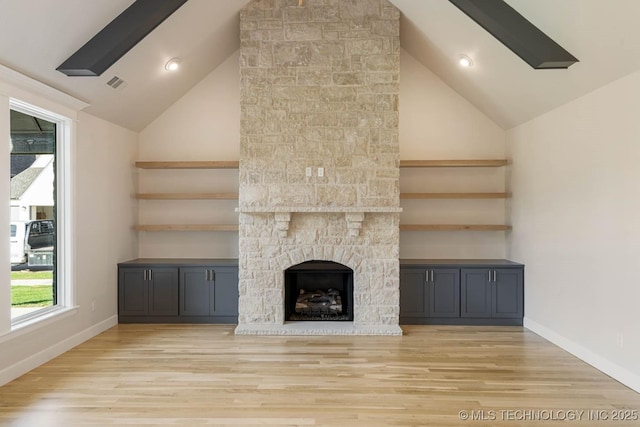 unfurnished living room with visible vents, wood finished floors, lofted ceiling with skylight, and a fireplace