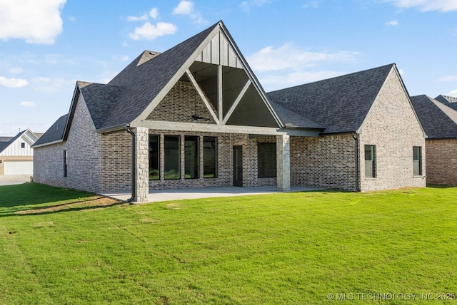 rear view of house featuring a lawn, brick siding, a patio area, and roof with shingles
