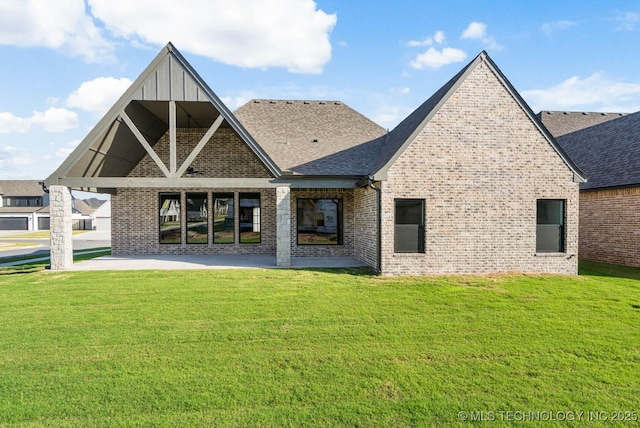 back of house featuring a lawn, brick siding, a shingled roof, and a patio area