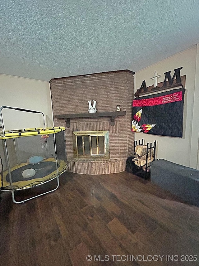 interior space with a brick fireplace, a textured ceiling, and wood finished floors
