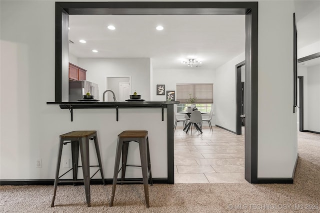 kitchen with light colored carpet, dark countertops, freestanding refrigerator, and a breakfast bar