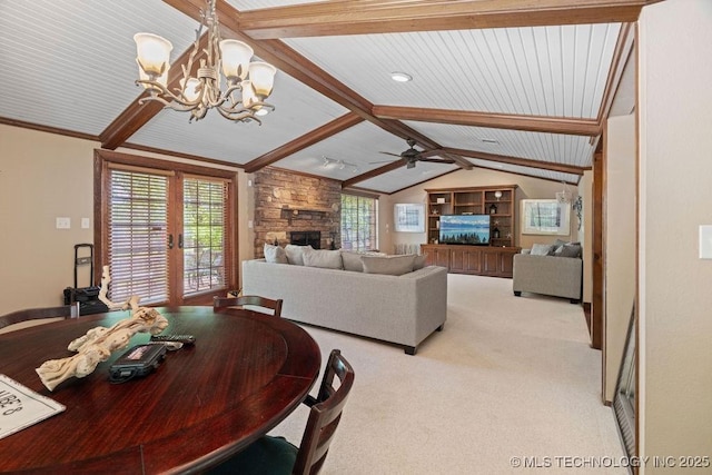 dining room with a stone fireplace, vaulted ceiling with beams, light colored carpet, french doors, and ceiling fan with notable chandelier