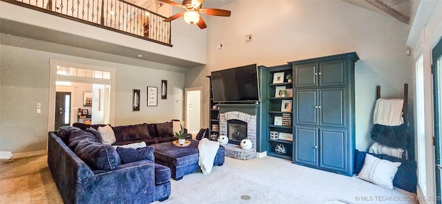 carpeted living room featuring ceiling fan, a fireplace, and a towering ceiling