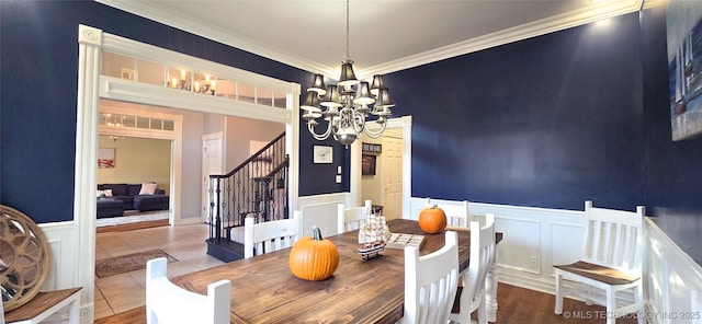 tiled dining room featuring crown molding, stairs, a decorative wall, a wainscoted wall, and a notable chandelier