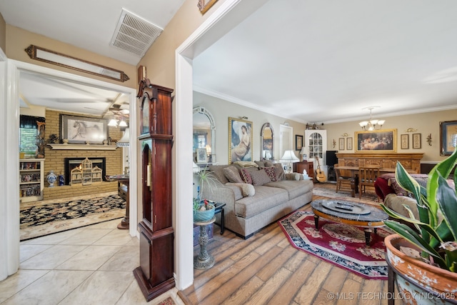 living area featuring ornamental molding, a notable chandelier, a brick fireplace, and visible vents