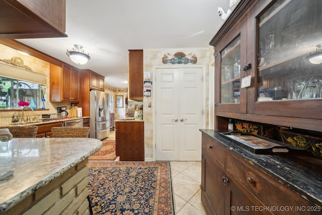kitchen with light tile patterned flooring, glass insert cabinets, light stone counters, a sink, and stainless steel appliances