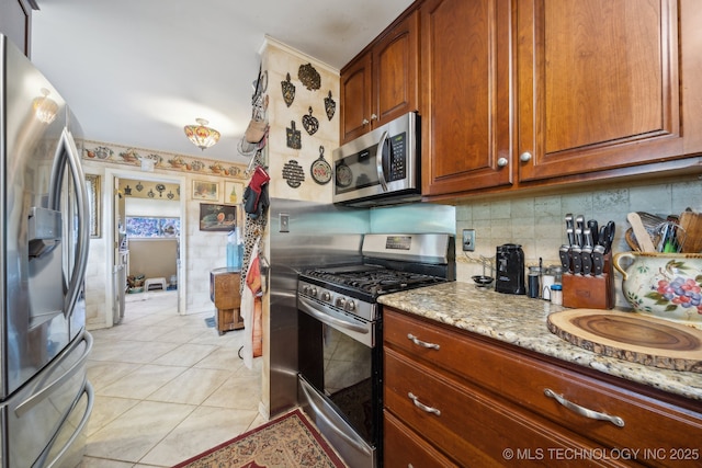 kitchen with brown cabinetry, light tile patterned flooring, light stone countertops, tasteful backsplash, and stainless steel appliances