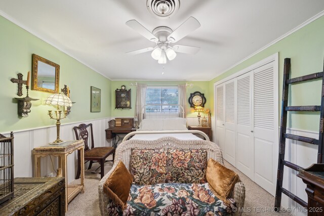 carpeted bedroom featuring ceiling fan, visible vents, crown molding, a wainscoted wall, and a closet