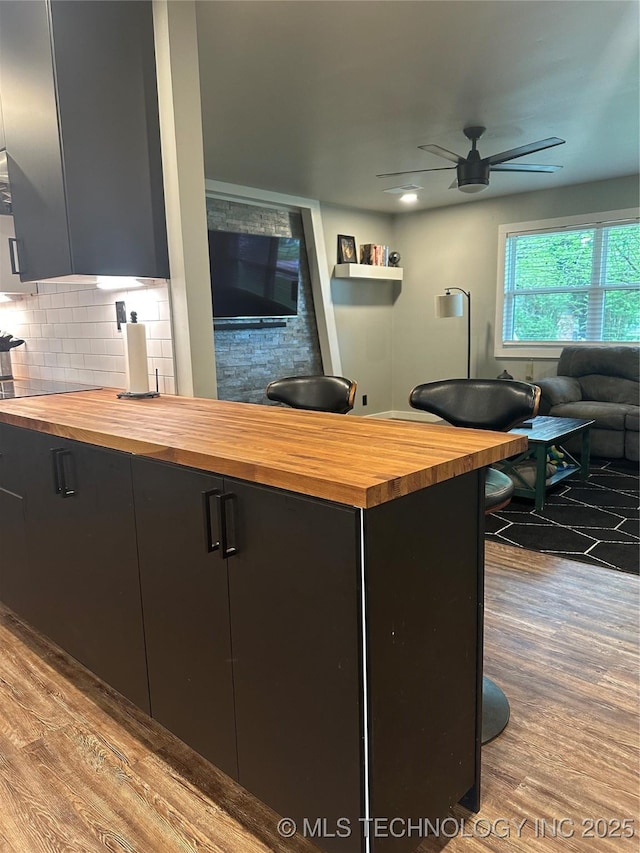 kitchen with butcher block counters, wood finished floors, open floor plan, ceiling fan, and tasteful backsplash