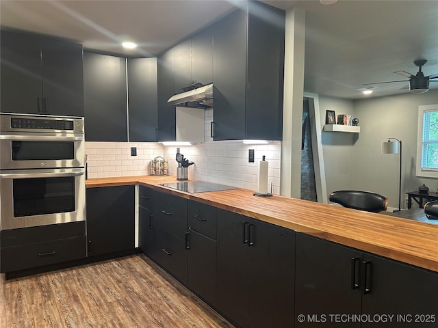 kitchen with dark cabinets, stainless steel double oven, black electric cooktop, and butcher block counters