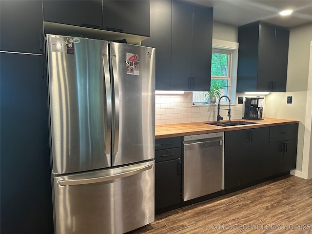 kitchen with decorative backsplash, appliances with stainless steel finishes, a sink, butcher block counters, and dark wood-type flooring