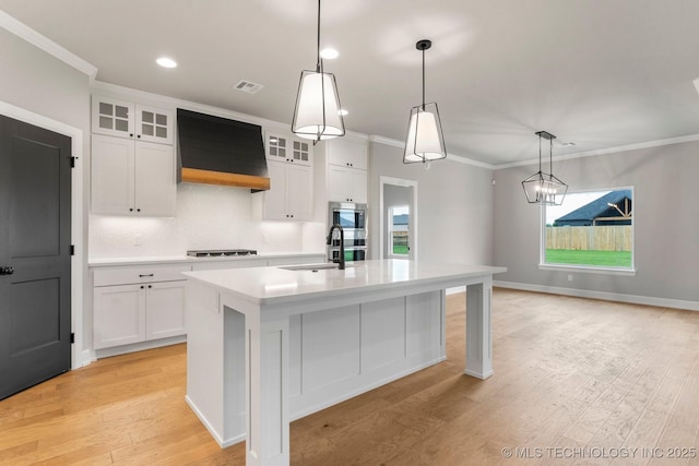 kitchen featuring crown molding, a sink, light countertops, an island with sink, and custom exhaust hood