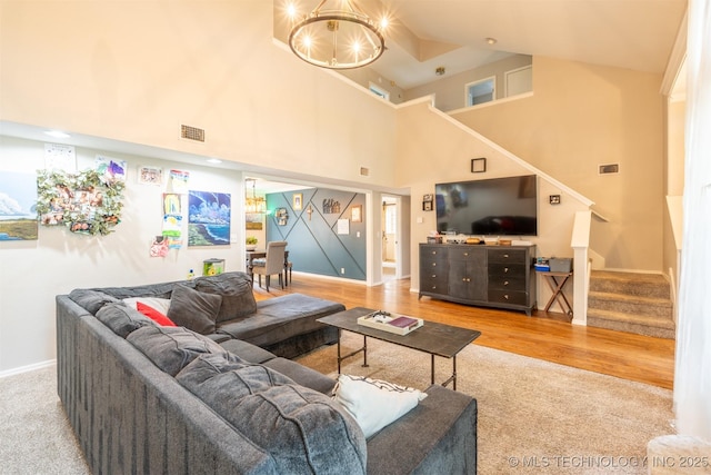 carpeted living area with visible vents, stairway, baseboards, an inviting chandelier, and a high ceiling