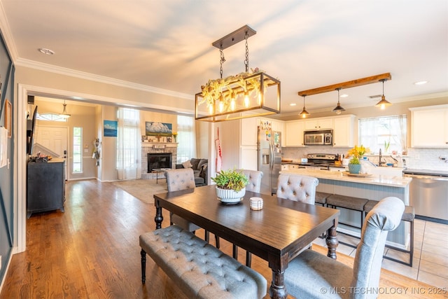 dining area featuring crown molding, light wood-type flooring, and a stone fireplace