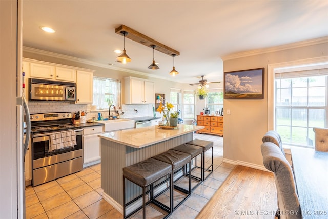 kitchen featuring decorative backsplash, a kitchen bar, a sink, white cabinets, and stainless steel appliances