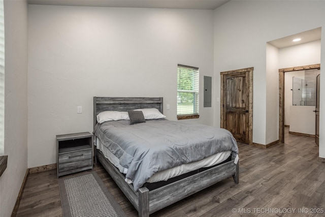 bedroom featuring wood finished floors, baseboards, a high ceiling, recessed lighting, and electric panel