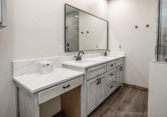 full bath with double vanity, a sink, wood finished floors, and a stall shower