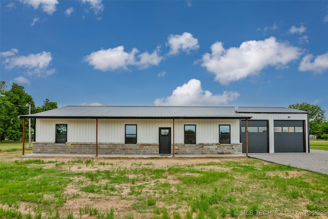 view of front of house with a garage, stone siding, gravel driveway, and metal roof
