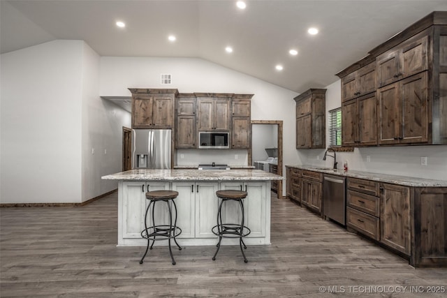 kitchen with a center island, a sink, lofted ceiling, a breakfast bar, and stainless steel appliances