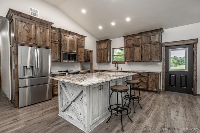 kitchen with visible vents, appliances with stainless steel finishes, a center island, vaulted ceiling, and wood finished floors