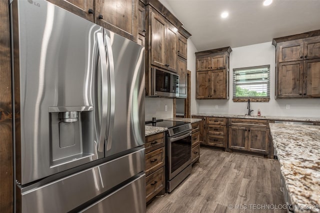 kitchen with light stone counters, a sink, stainless steel appliances, recessed lighting, and wood finished floors