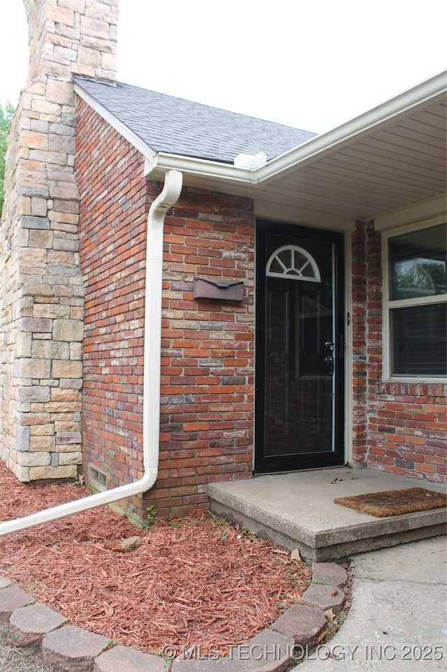 view of exterior entry with brick siding and a shingled roof