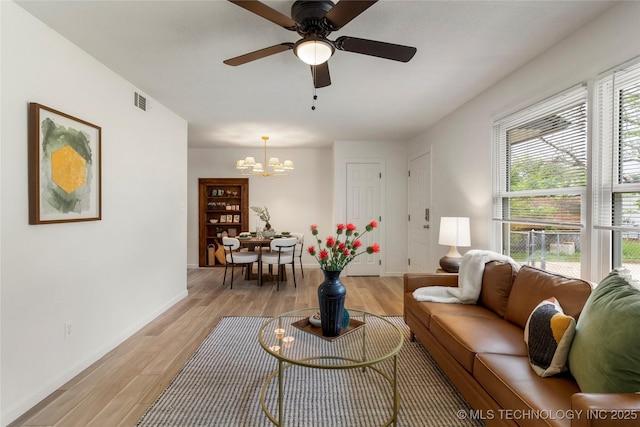 living room featuring baseboards, visible vents, ceiling fan with notable chandelier, and light wood-type flooring