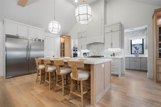kitchen with a kitchen island with sink, tasteful backsplash, light countertops, high vaulted ceiling, and stainless steel built in refrigerator