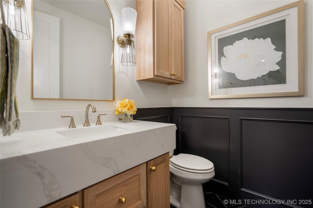 bathroom featuring vanity, wainscoting, toilet, and a decorative wall