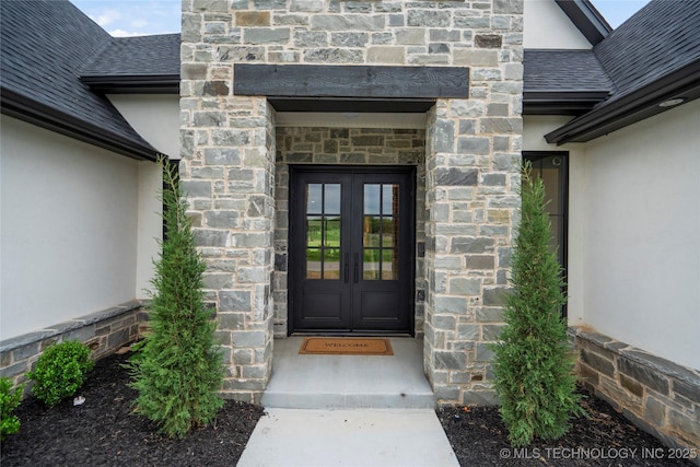 entrance to property featuring french doors, stucco siding, a shingled roof, and stone siding