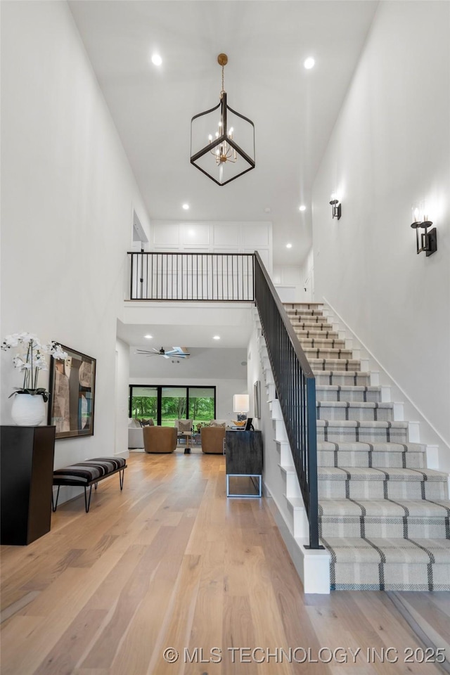 stairs featuring an inviting chandelier, recessed lighting, a towering ceiling, and wood finished floors