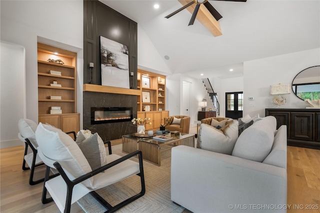 living room featuring built in features, a fireplace, high vaulted ceiling, a ceiling fan, and light wood-style flooring