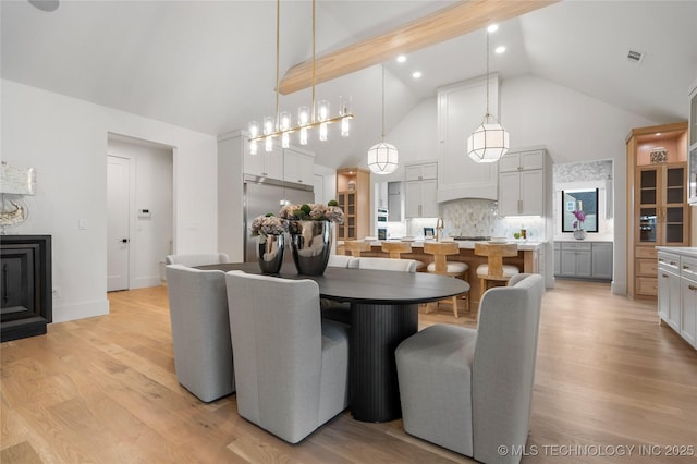 dining room with high vaulted ceiling, a fireplace, light wood-type flooring, and visible vents