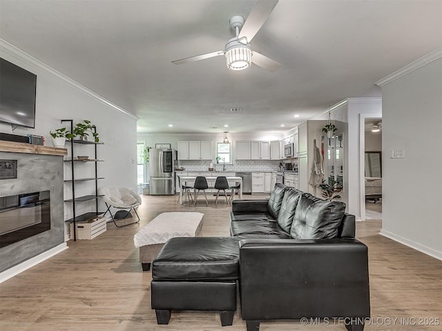 living area featuring crown molding, baseboards, ceiling fan, and a tiled fireplace