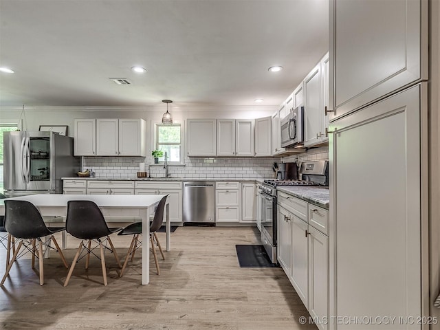 kitchen with visible vents, decorative backsplash, ornamental molding, light wood-style flooring, and appliances with stainless steel finishes