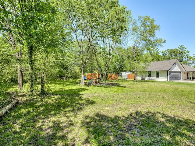 view of yard with fence, an attached garage, and a playground