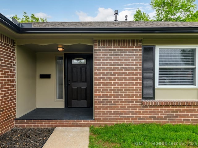 view of exterior entry with brick siding and roof with shingles