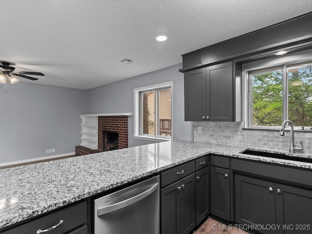 kitchen featuring stainless steel dishwasher, a sink, visible vents, and light stone countertops