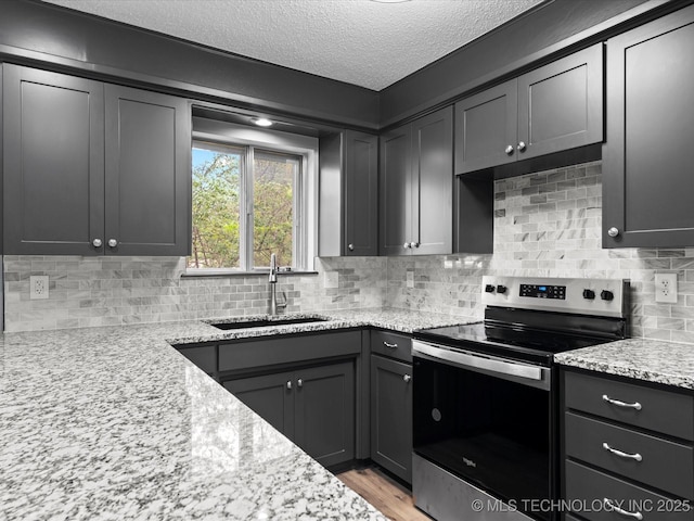 kitchen featuring stainless steel range with electric stovetop, a textured ceiling, tasteful backsplash, light stone counters, and a sink