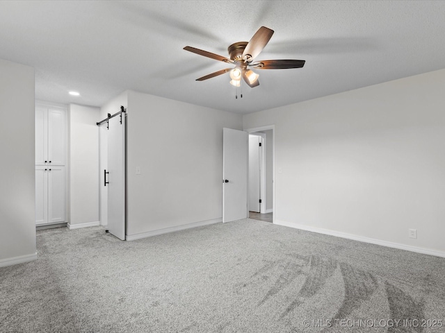 interior space with a barn door, ceiling fan, light carpet, and baseboards