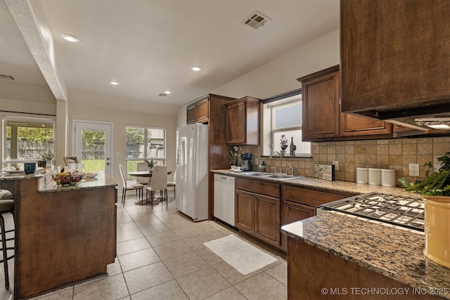kitchen with a breakfast bar, a sink, white appliances, backsplash, and visible vents