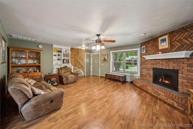 living room featuring ceiling fan, visible vents, a fireplace, light wood-style floors, and stairs
