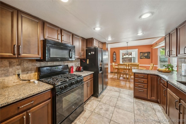 kitchen featuring backsplash, black appliances, brown cabinets, and light stone countertops