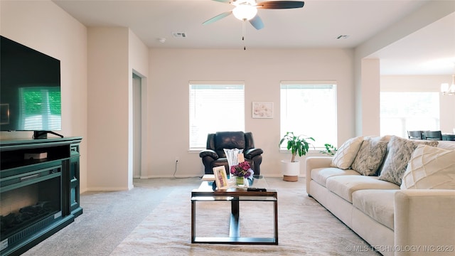 living room featuring baseboards, ceiling fan with notable chandelier, light colored carpet, and visible vents